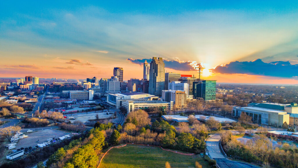 Aerial view of a city skyline at sunset with buildings, trees, and a green park in the foreground.